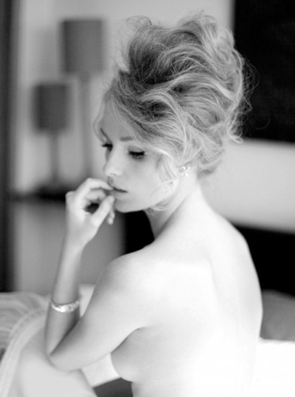 Black and white portrait of an adult woman with an elaborate hairstyle, bare shoulders, and a bracelet in an indoor setting with soft lighting.