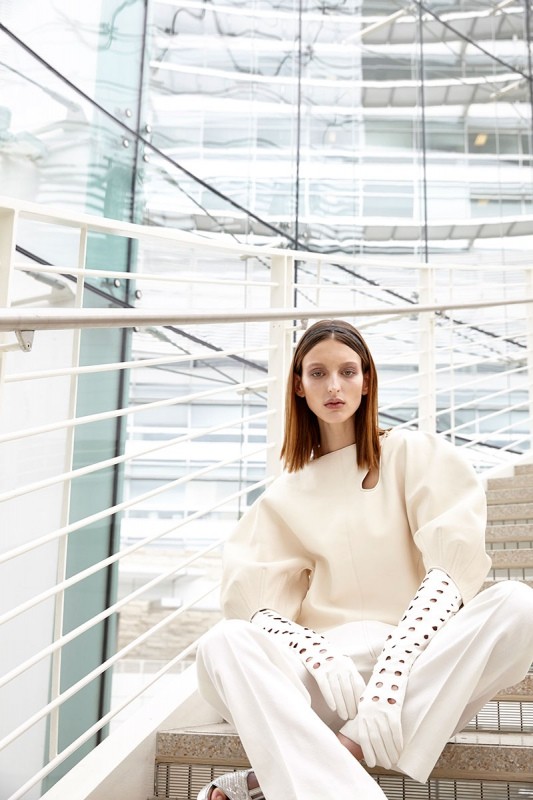 Fashion shot of woman in white outfit sitting on stairs in front of a modern building with glass walls. Style and indoor setting.