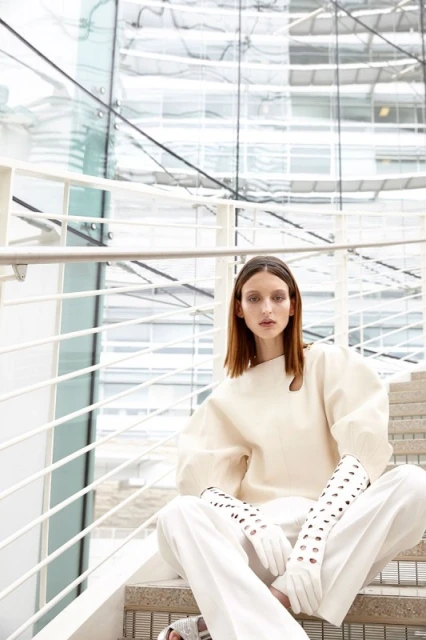 Fashion shot of woman in white outfit sitting on stairs in front of a modern building with glass walls. Style and indoor setting.