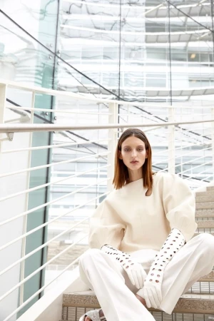 Fashion shot of woman in white outfit sitting on stairs in front of a modern building with glass walls. Style and indoor setting.