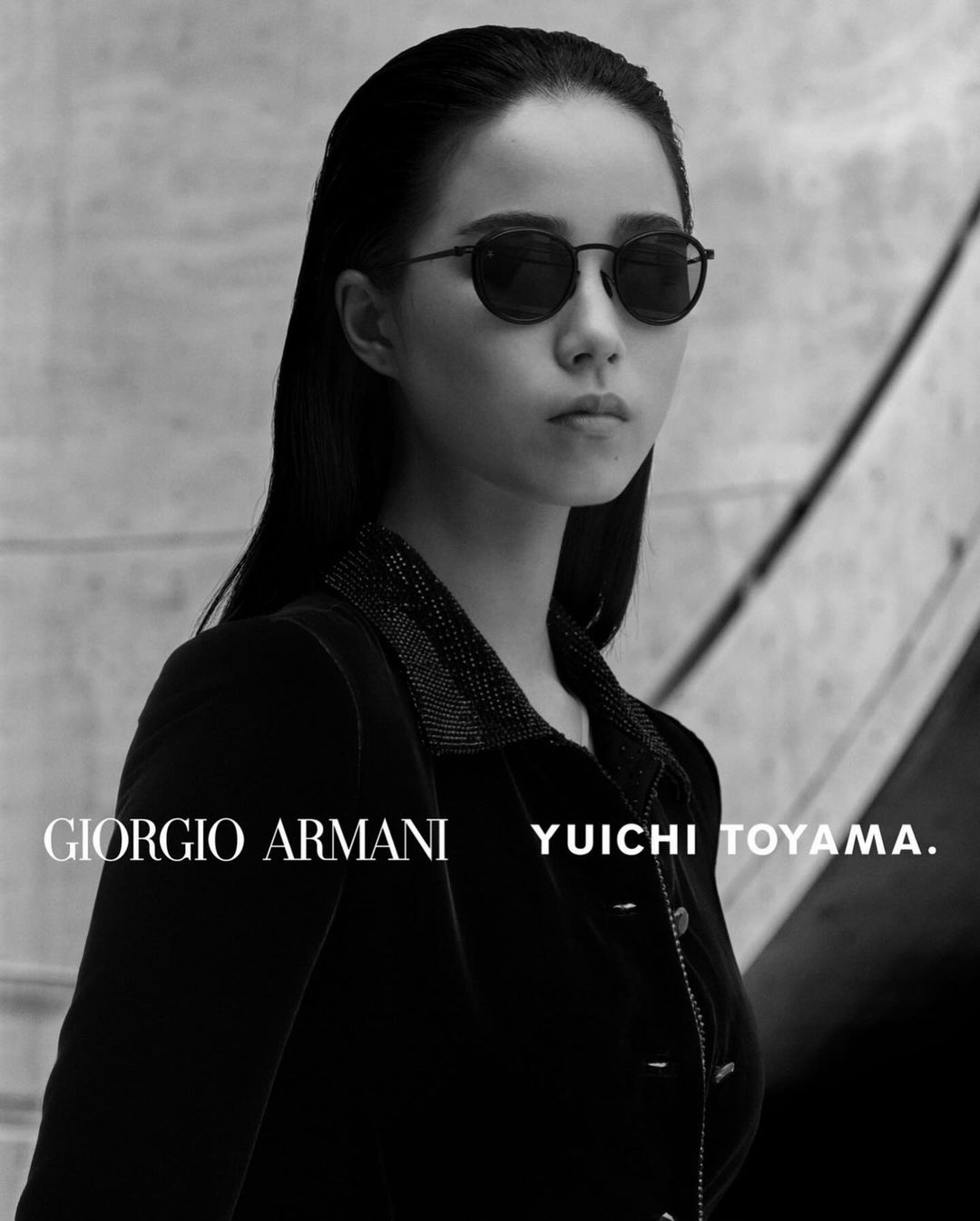 Black-and-white portrait of an Asian woman wearing sunglasses and a dark jacket, with the Giorgio Armani logo visible in the foreground.