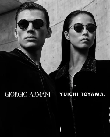 Black and white portrait of a man and woman wearing dark round sunglasses against a textured concrete wall