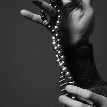 Monochrome close-up of hands holding a long strand of lustrous pearls and a textured knit sleeve.