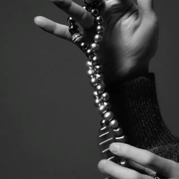 Monochrome close-up of hands holding a long strand of lustrous pearls and a textured knit sleeve.
