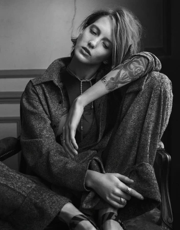 Black and white portrait of a woman with a tattoo on her arm sitting in a chair wearing a patterned matching shirt and pants