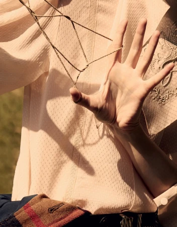 Woman's hand playing cat's cradle with string, wearing a light pink blouse, captured in natural light with a blurred background.