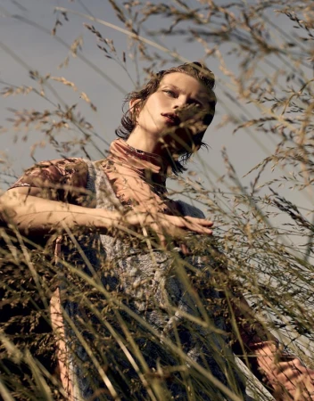 Model framed by tall grass looking upward in an outdoor editorial portrait photographed by Takay