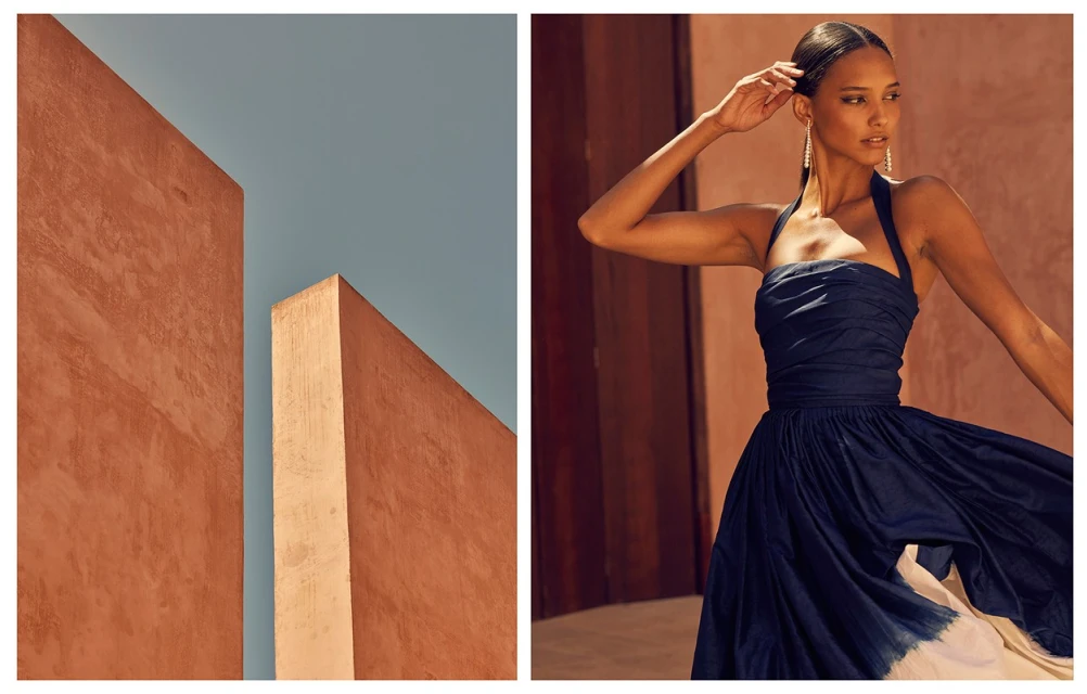 Fashion shot of a woman wearing a dark blue dress with a halter top, posing against a backdrop of orange walls and blue sky.