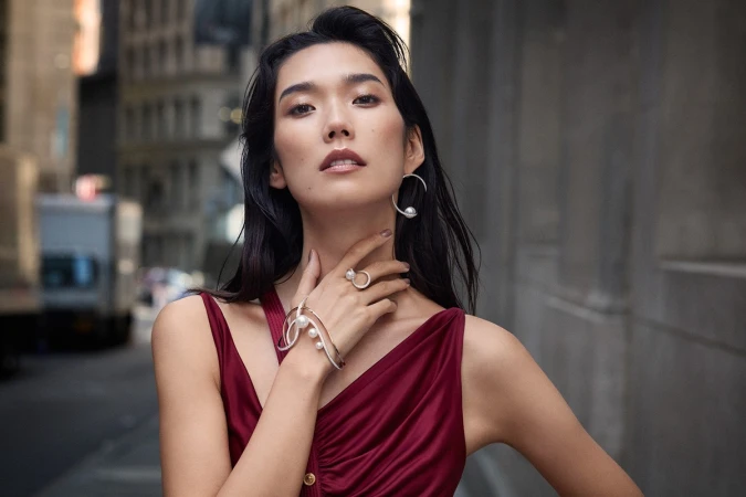 Woman in a burgundy dress wearing pearl jewelry posing on a city street, photographed by Takay