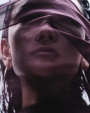 Close-up portrait of a person with a purple sheer fabric draped across their face and eyes, photographed by Takay.