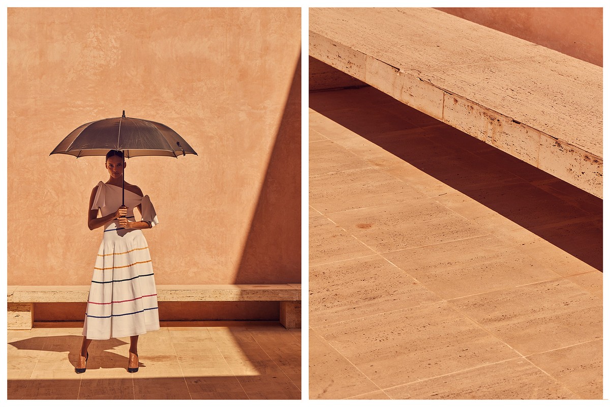 An adult female stands in sunlight under an umbrella, wearing a striped skirt, with a peach-toned wall behind, split-view with travertine surface.