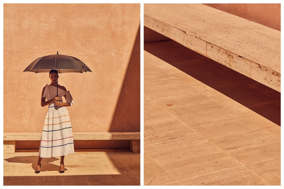 An adult female stands in sunlight under an umbrella, wearing a striped skirt, with a peach-toned wall behind, split-view with travertine surface.