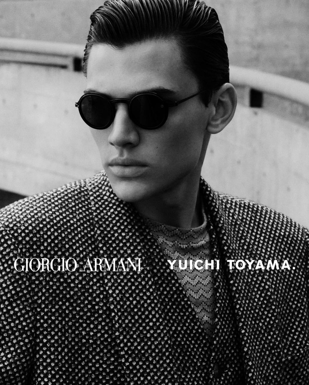 Monochrome close-up of a man wearing sunglasses and a patterned jacket, featuring 'Giorgio Armani' and 'YUICHI TOYAMA' text.