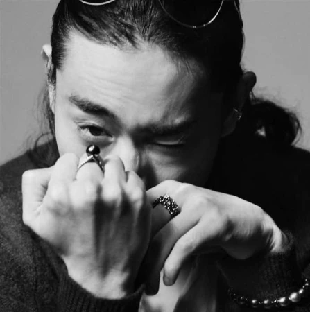 Close-up black and white portrait of a man wearing rings, posing with hands up to his face by photographer Takay.