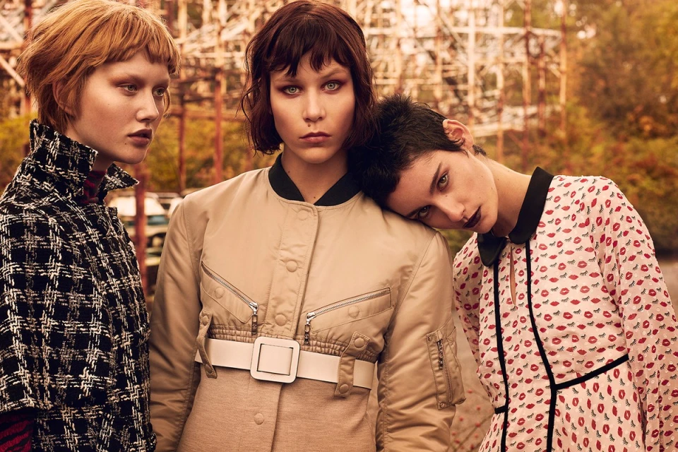 Three fashion models in an outdoor setting, styled with unique haircuts and distinct patterned and colored clothing, posing in a group.