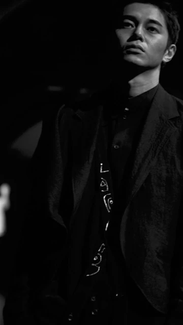 Monochrome portrait of an adult male wearing a suit jacket and button-down shirt, looking up and to the side in low lighting conditions.