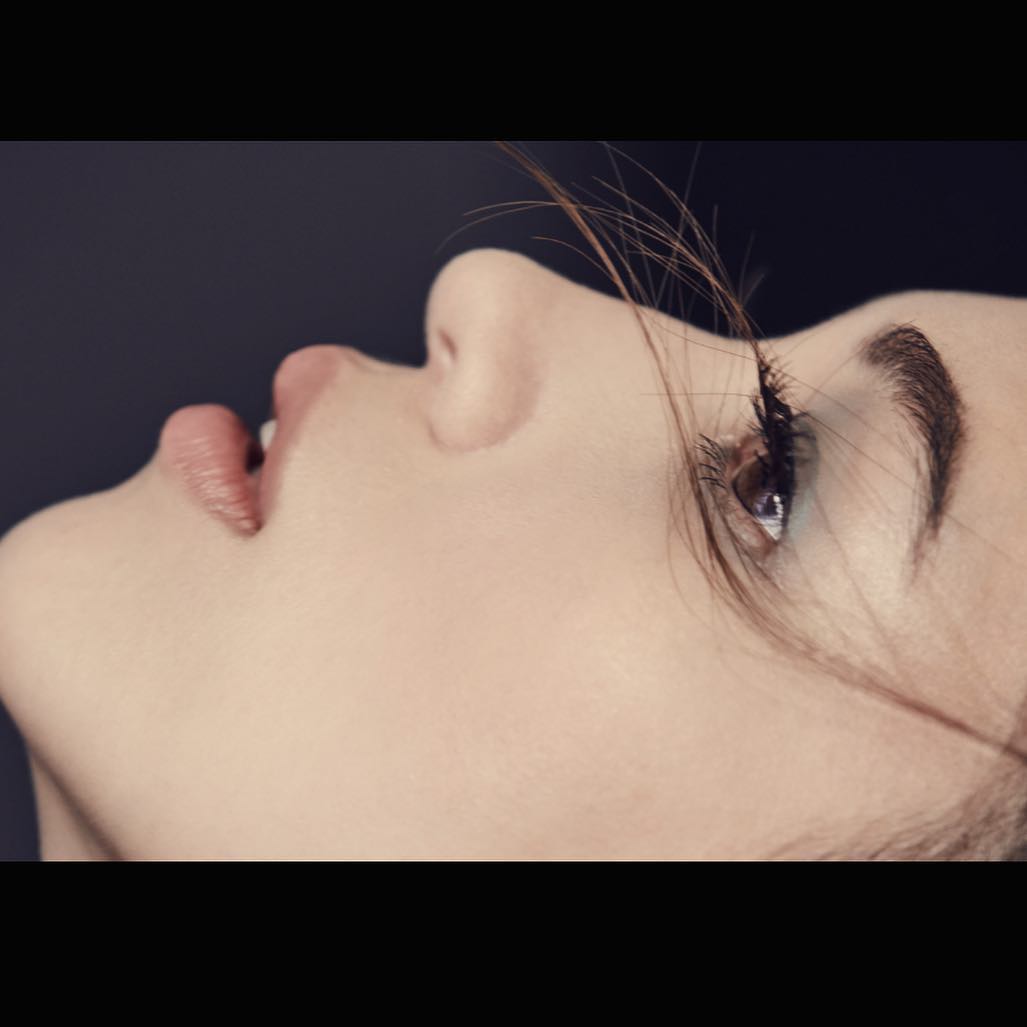 Extreme close-up profile shot of a woman face with dark hair strands across her eye and dark background