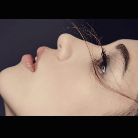 Extreme close-up profile shot of a woman face with dark hair strands across her eye and dark background