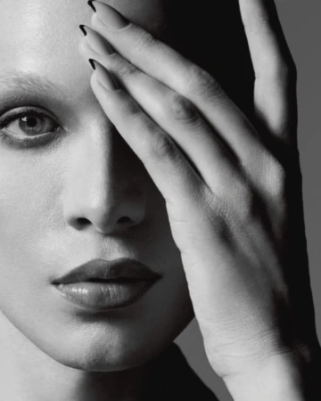Monochrome portrait of a woman with hand covering part of her face, showcasing her glossy lips and manicured nails.