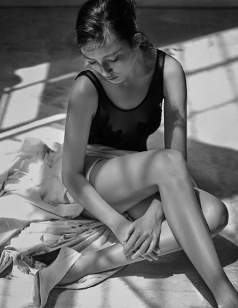 Monochrome portrait of a seated woman wearing a dark top, captured in natural angled light by photographer Takay.