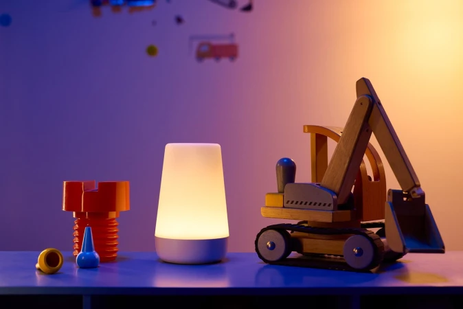 Stylized product shot of a lit white noise machine, wooden construction toy, and building blocks on a blue surface against a split tone background.
