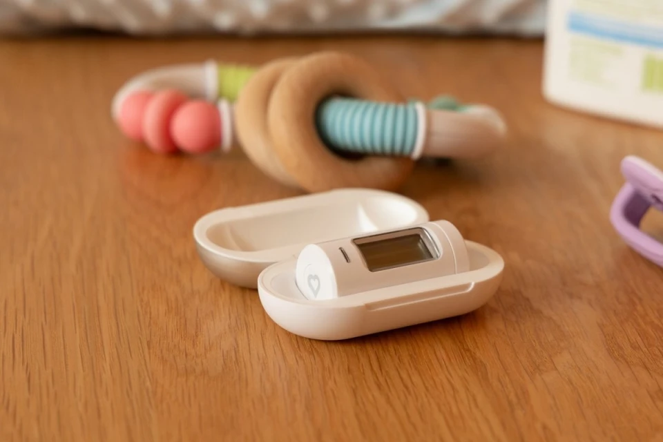 Close-up of a baby monitor device in its case on a wood surface, accompanied by a wooden toy and a purple clip.