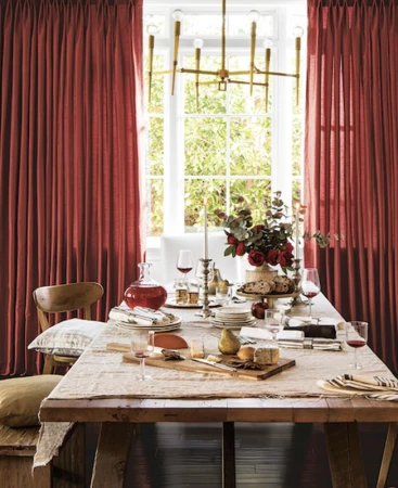 Dining table set with a linen tablecloth, glassware, and floral centerpiece, illuminated by a modern chandelier in a bright room.