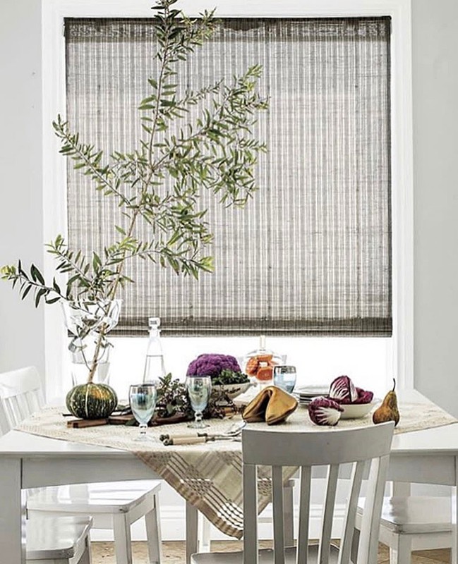 Dining table setting with green foliage, pumpkin, fortune cookies, glasses, and decorative tableware in a well-lit indoor space.