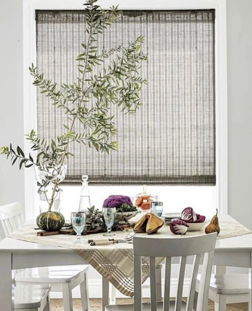 Dining table setting with green foliage, pumpkin, fortune cookies, glasses, and decorative tableware in a well-lit indoor space.