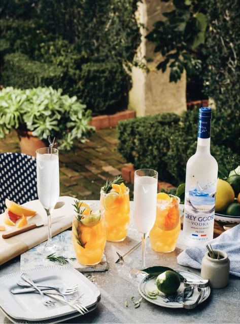 Grey Goose vodka bottle and crafted cocktails with citrus garnish on table in outdoor garden setting, showcasing beverage photography.