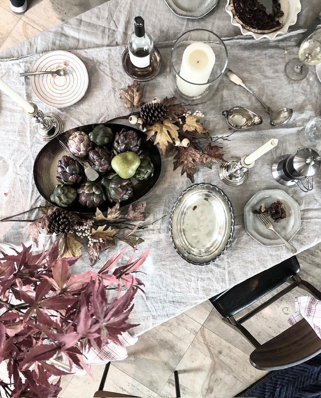 Overhead shot of a linen-covered table set with silver cutlery, glassware, candles, and a fruit and artichoke centerpiece.