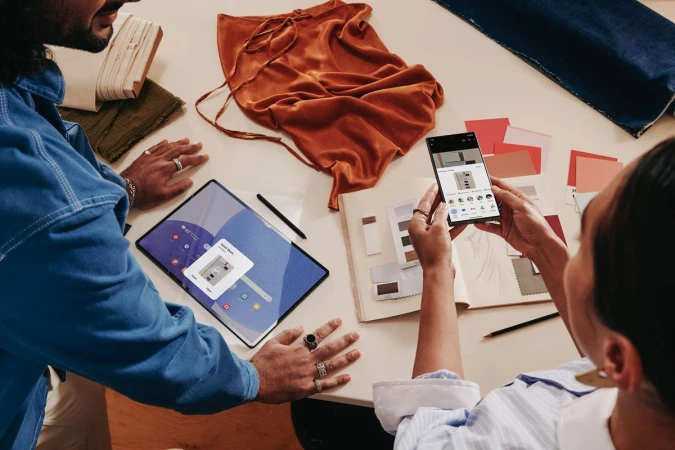 Two people at table with tablet and smartphone showcasing design work; modern technology and creative collaboration in studio setting.