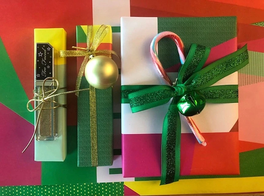 Festive holiday image featuring three wrapped gifts, including Too Faced makeup. They are decorated with ribbon, an ornament, and a candy cane.