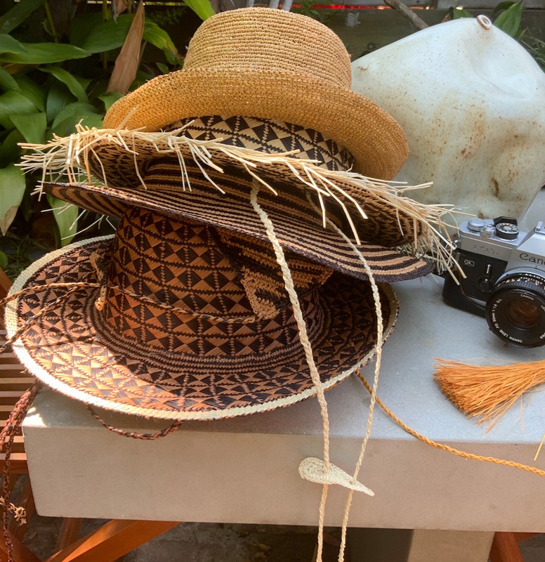 Stack of three straw hats with patterned bands displayed outdoors next to a vintage camera and a white ceramic object.