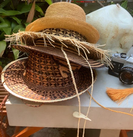 Stack of three straw hats with patterned bands displayed outdoors next to a vintage camera and a white ceramic object.
