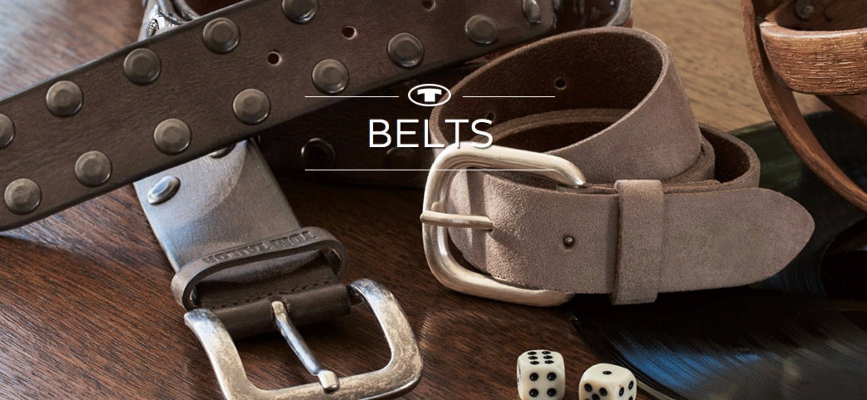 Two brown leather belts with metal buckles are displayed alongside dice on a dark wooden surface, captured in a studio setting.