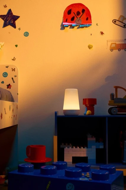 Kids' bedroom at night with a lamp illuminating toys, bed, and decorations on the wall, creating a warm and playful scene.