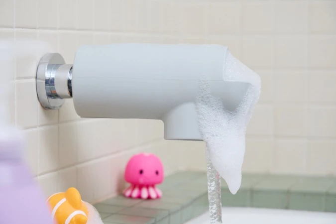 A close-up showcases a faucet with a foam spout and water running, complemented by two children's bath toys.