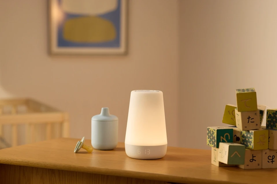 Glowing nightlight and baby accessories on a wooden table, including a sippy cup, pacifier, and wooden alphabet blocks in a nursery setting.