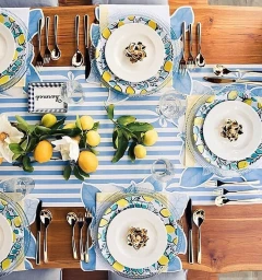 Overhead view of a dining table styled with lemon-patterned plates, blue and white striped runner, and fresh lemons.