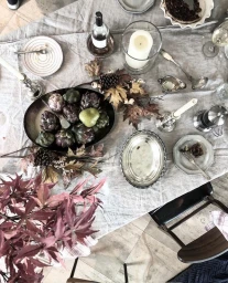 Overhead view of an autumn dining table styled with linen tablecloth, artichokes, and seasonal leaves by Tam Reid.