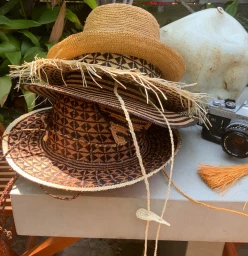 A stack of woven straw hats with geometric patterns rests on a concrete surface next to a vintage camera.