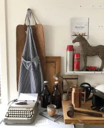 Still life interior set design featuring a vintage typewriter, striped apron, and decorative props by Tam Reid.