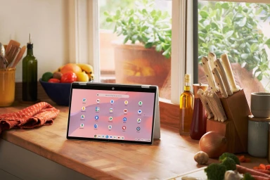 Silver laptop displaying app icons set on a wooden kitchen counter with a knife block, oil bottles, and a fruit bowl.