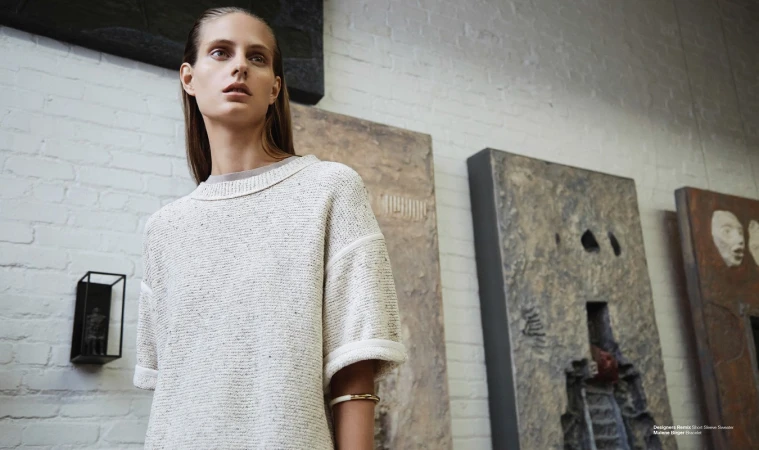 Adult woman wearing a knit sweater in a photo studio with art on the walls. Portrait-style shot for fashion or editorial content.