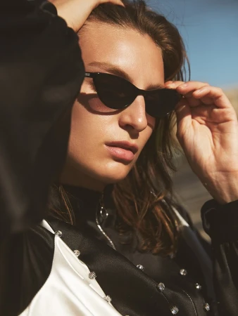 Woman poses outdoors wearing sunglasses and black and white clothing. Fashion style portrait with warm lighting and blue sky.