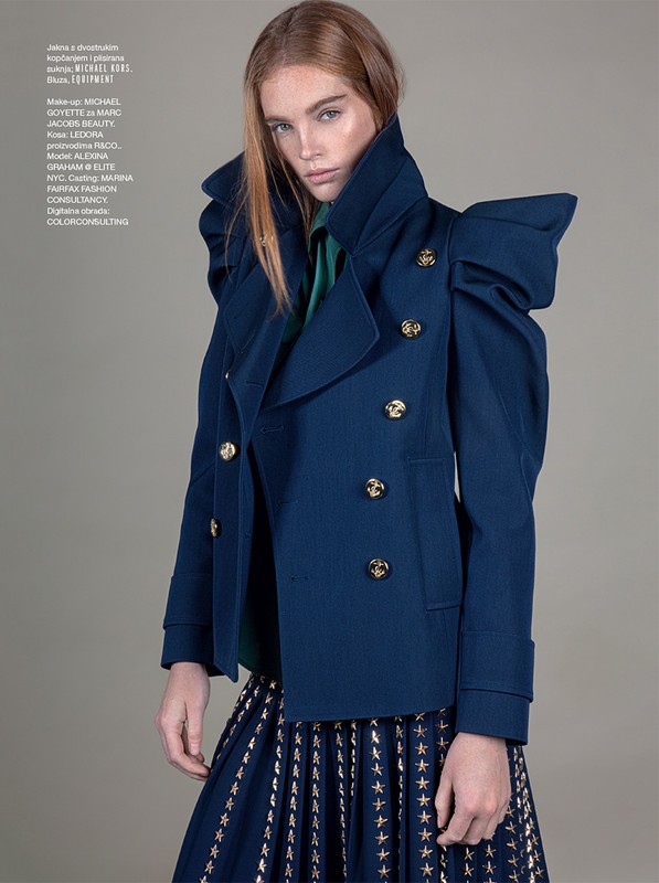 Fashion editorial shot: A red-haired woman poses in a studio wearing a striking blue jacket with oversized shoulder pads and a star-patterned skirt.