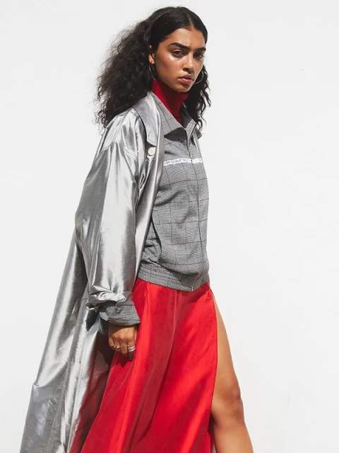Woman in a gray plaid top and red skirt with a silver jacket poses in a fashion shot against a white backdrop in a studio.