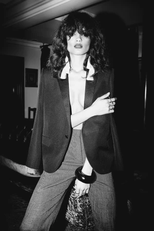 Black and white portrait of a woman wearing a dark blazer over a collared shirt and trousers, styled by Tatiana Cinquino.