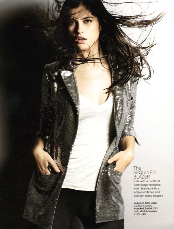Woman posing in a sequined blazer, white top, and black pants. Fashion photography with a dark background and studio lighting.